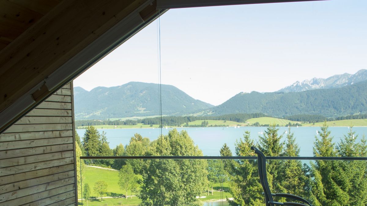 Blick vom Bett der Ferienwohnung durch das Panoramafenster über den Forggensee auf die Allgäuer und Ammergauer Berge